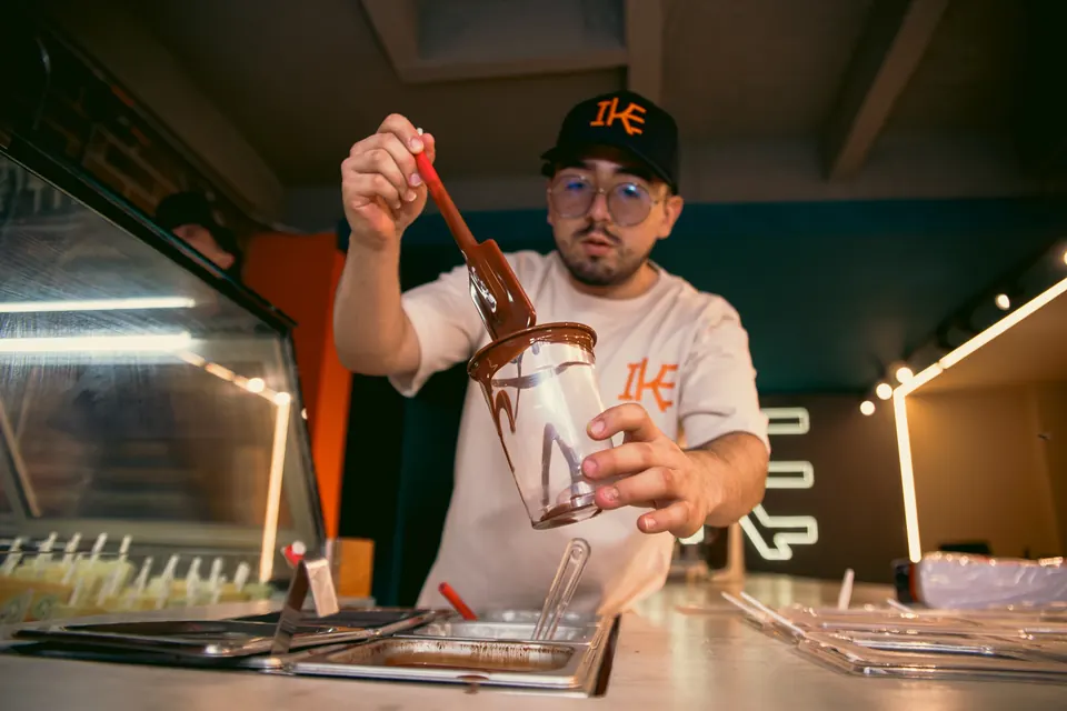 Miembro del equipo IKE bañando una paleta en chocolate en la barra del local