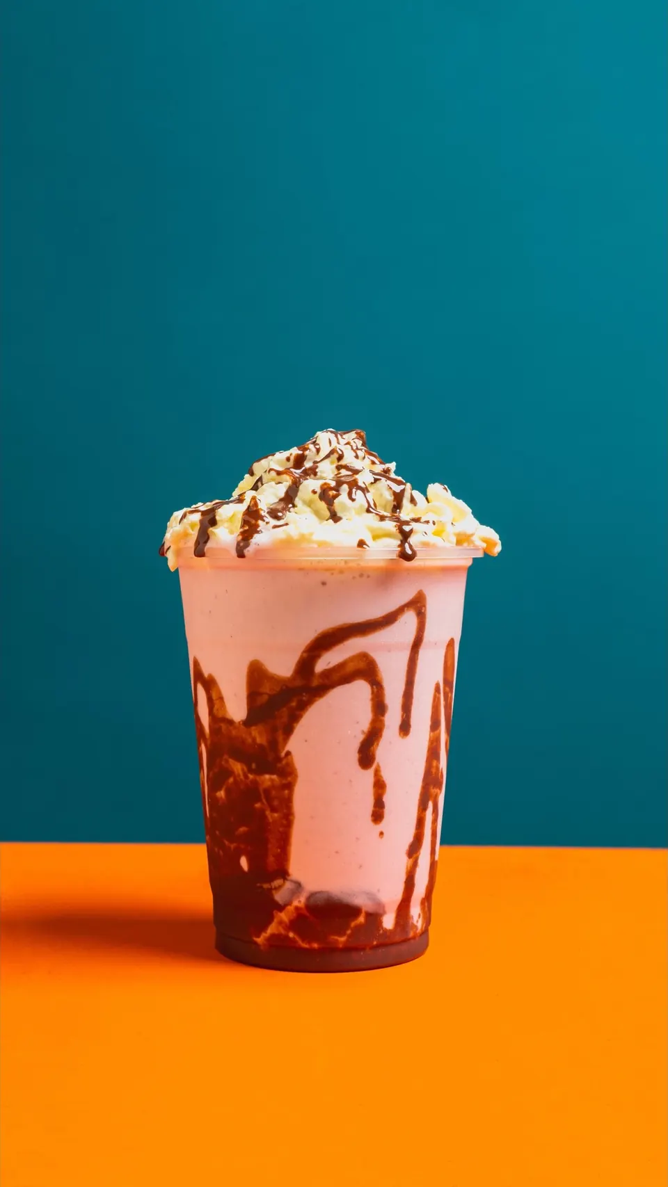 Malteada IKE con chantilly y chocolate chorreado en el vaso, sobre fondo azul y naranja